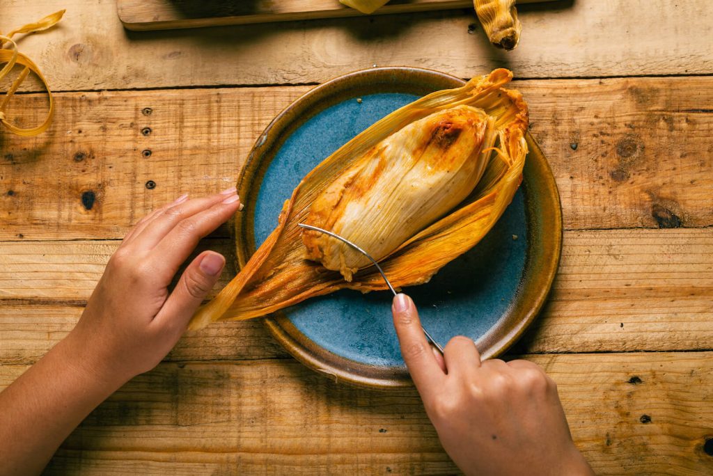 hands of a person cutting a tamale with a fork
